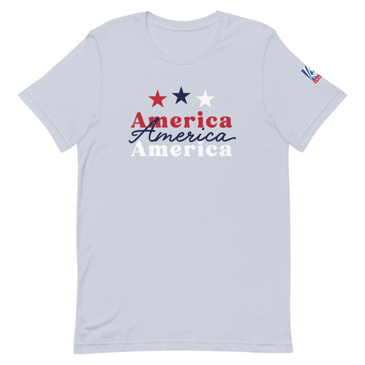A proud American man wearing the light blue FOX News America t-shirt in a modern, sunlit American living room setting.