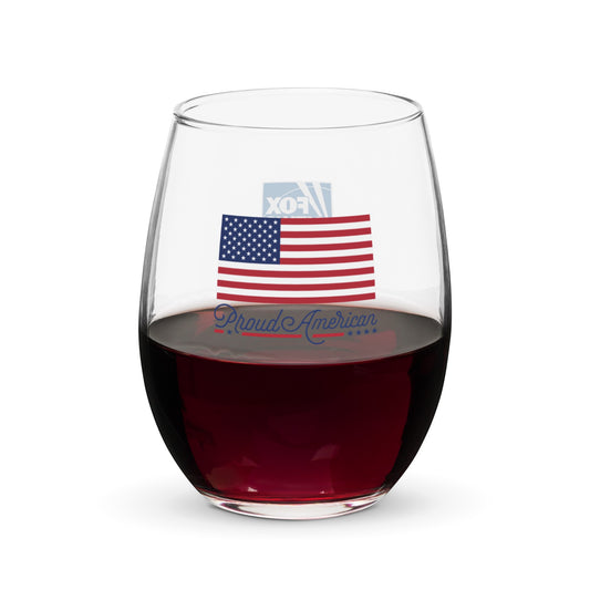 A clear FOX News Proud American stemless wine glass featuring a crisp logo, sitting on a wooden table in a sunlit American kitchen.