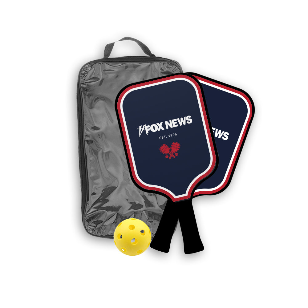 A premium *FOX News* Logo Pickleball Set featuring two navy blue paddles with the iconic logo and two yellow balls, displayed on a clean suburban patio table in a bright, outdoor morning setting.