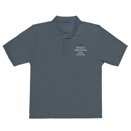 A modern American living room background showcasing the front view of the FOX News Proud American Dad embroidered polo shirt in Cool Heather.