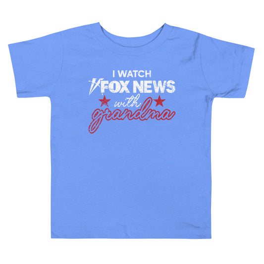A toddler in a suburban American home wearing a pink FOX News shirt that says I Watch with Grandma.
