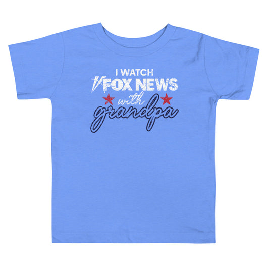 A toddler smiling while wearing the FOX News I Watch with Grandpa graphic t-shirt in a bright suburban living room setting.