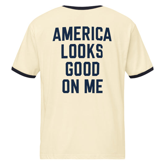 White ringer t-shirt with red contrast trim, featuring the Fox News America Looks Good On Me graphic centered on the chest in a clean suburban living room setting