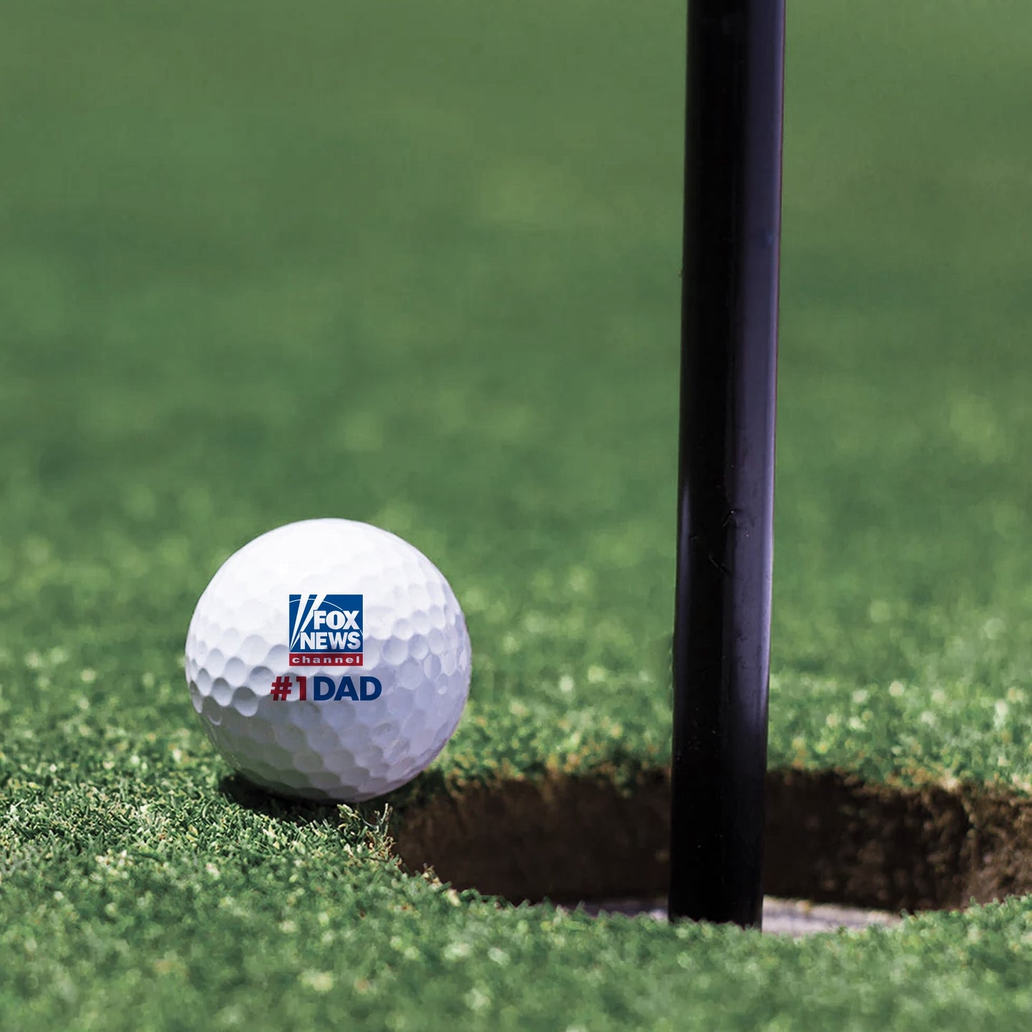 FOX News Dad golf balls displayed next to a golf club on a green lawn in a clean backyard setting.
