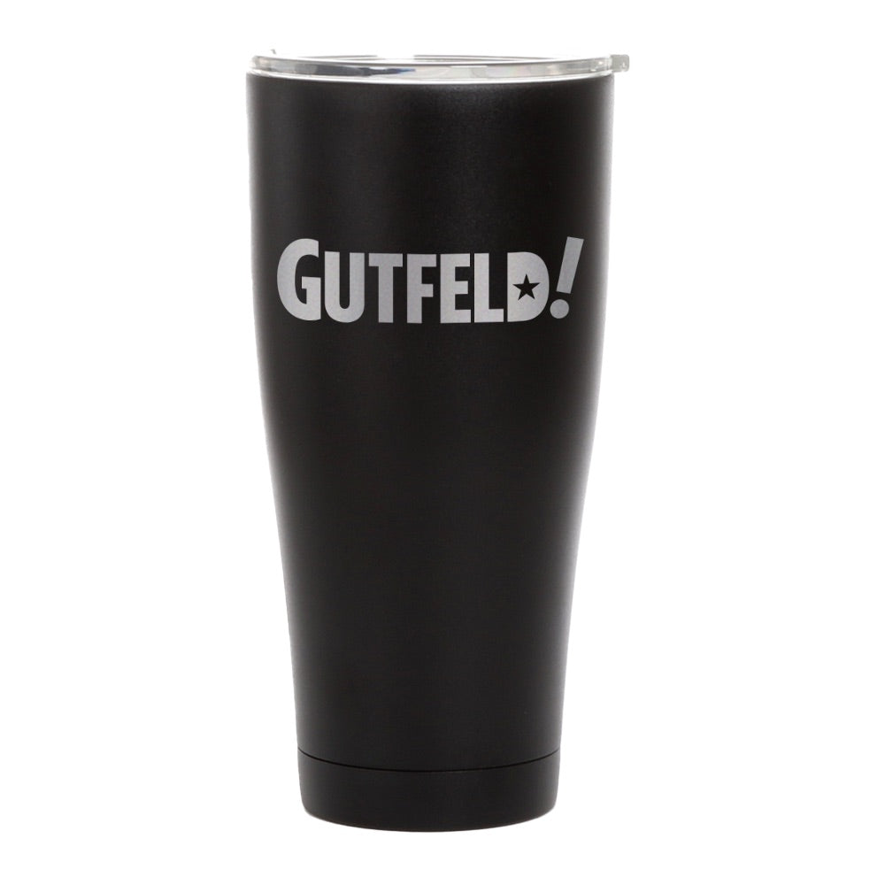 A close-up of the Gutfeld! logo on a matte black 20 oz insulated tumbler standing on a wooden coffee table.