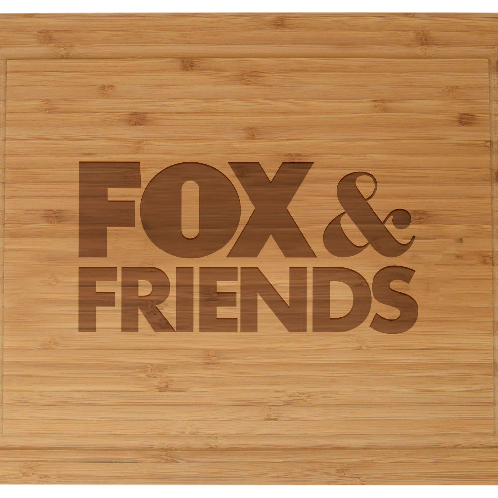 Close up shot of the crisp laser engraved *FOX & Friends* logo on the natural wood surface of the cutting board.