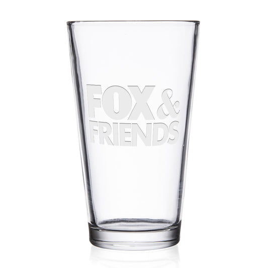 A personalized *FOX & Friends* laser engraved pint glass sitting on a clean wooden coaster in a bright, modern American kitchen.