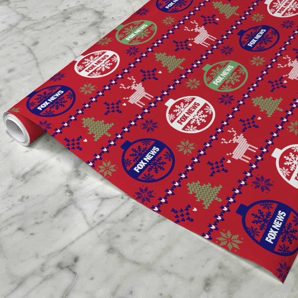 A roll of FOX News logo holiday wrapping paper displayed on a clean wooden table in a comfortable American home.