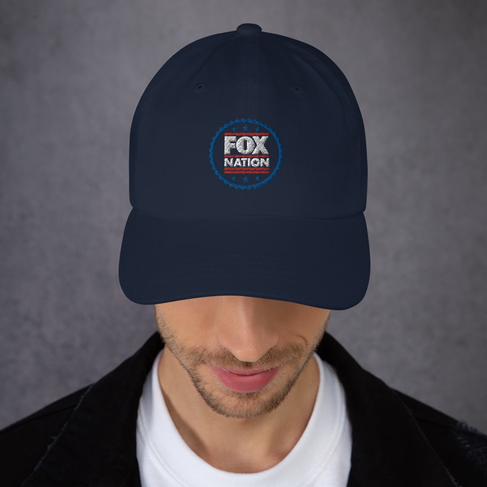 A patriotic American man wearing the FOX Nation embroidered hat while enjoying a morning coffee in a tidy suburban backyard.