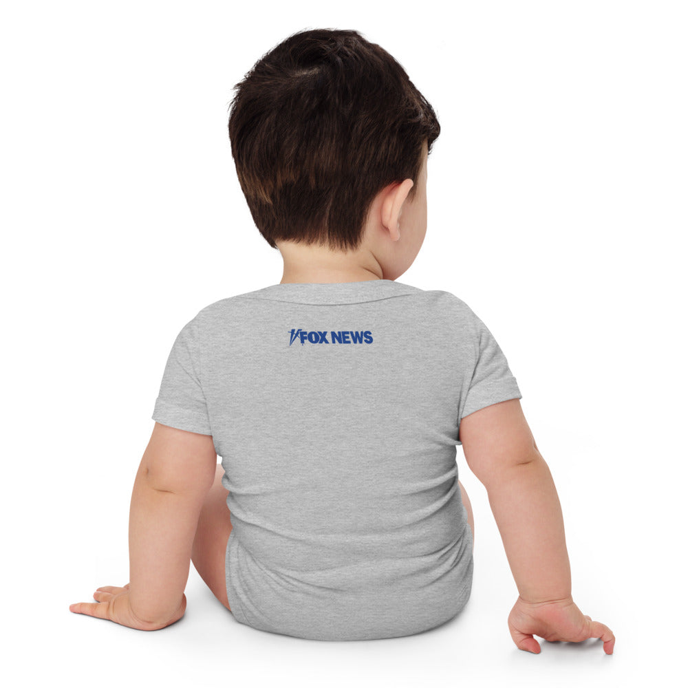 A white FOX News baby bodysuit displayed on a clean wooden surface in a well-lit suburban home.