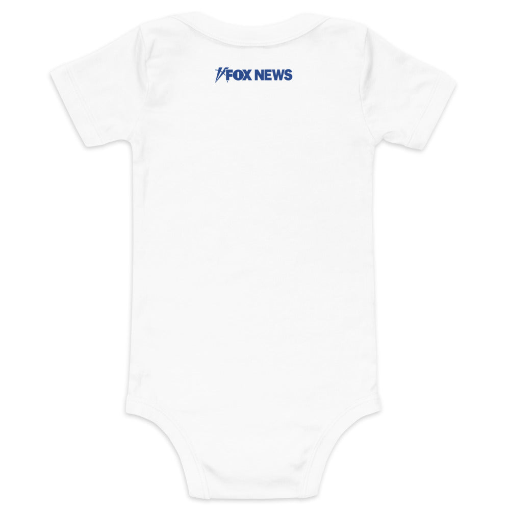 A gift-wrapped FOX News baby bodysuit next to a morning coffee mug in a cozy home setting.