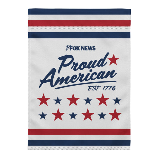 Official FOX News Proud American Est. 1776 Garden Flag displayed on a black metal stand in a well-manicured American suburban garden.