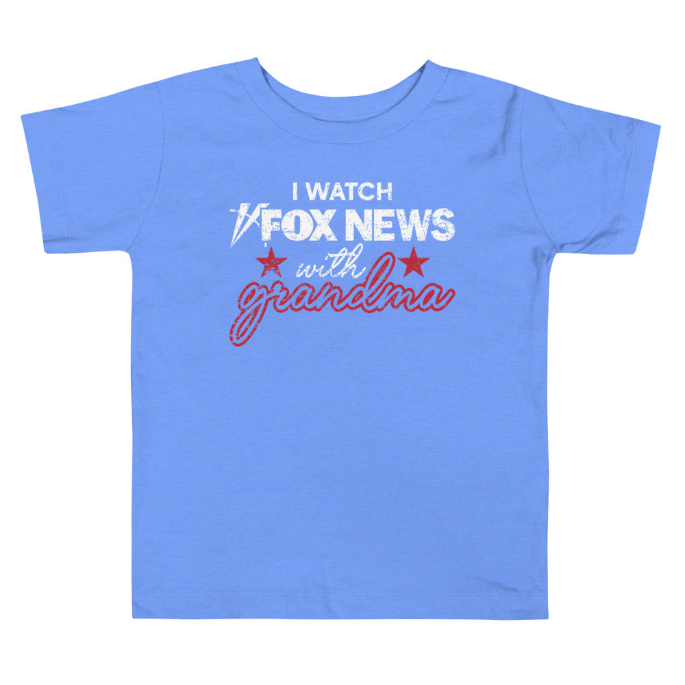 A toddler in a suburban American home wearing a pink FOX News shirt that says I Watch with Grandma.