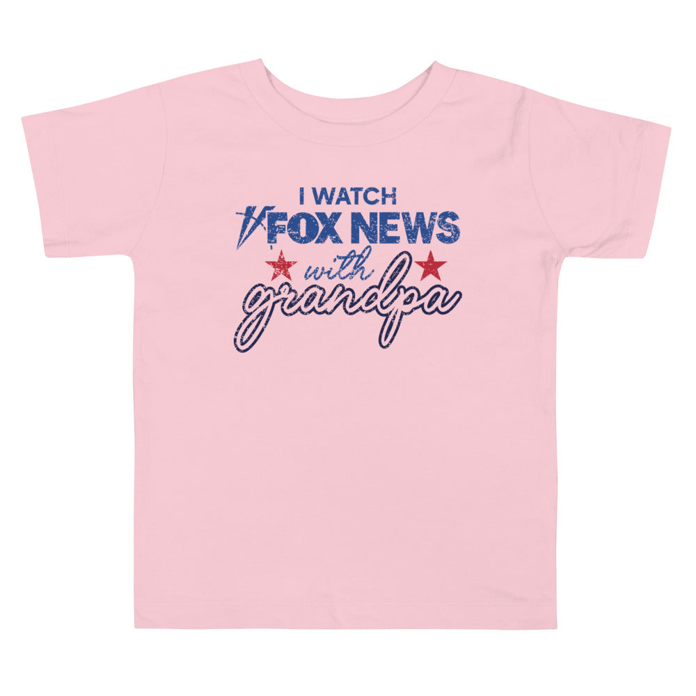 A cheerful toddler modeling the FOX News youth apparel against a clean, warm-toned background.