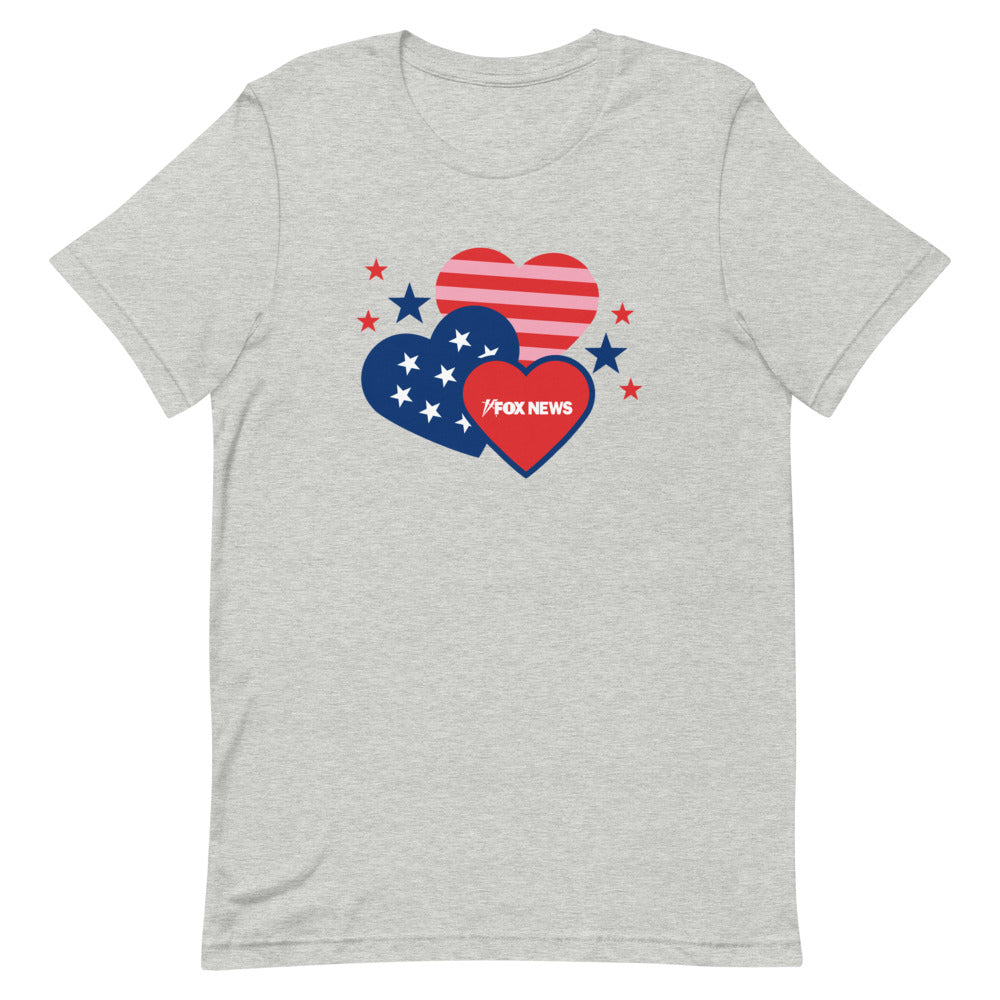A Caucasian woman wearing the white *FOX News* Hearts Unisex T-Shirt in a clean, modern American living room, highlighting the crisp logo design.