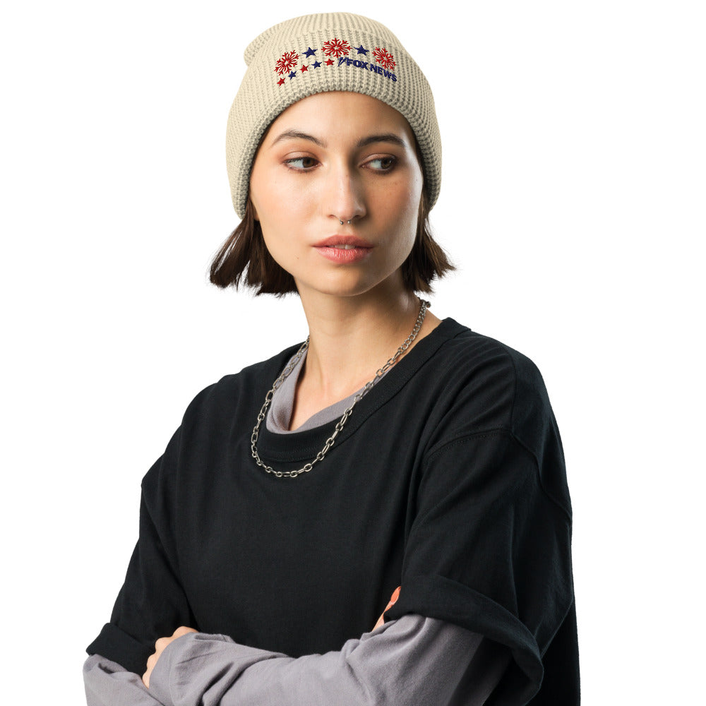 The Camel colored FOX News Holiday Snowflakes Beanie displayed on a wooden table near a window.
