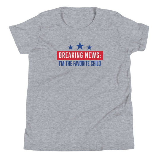 A young child wearing the FOX News Breaking News Kids T-Shirt in Athletic Heather standing in a bright, modern American backyard.