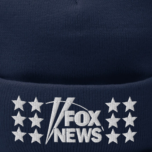 A close-up of the FOX News logo embroidered on a navy blue pom pom beanie in a clean American home setting.-1
